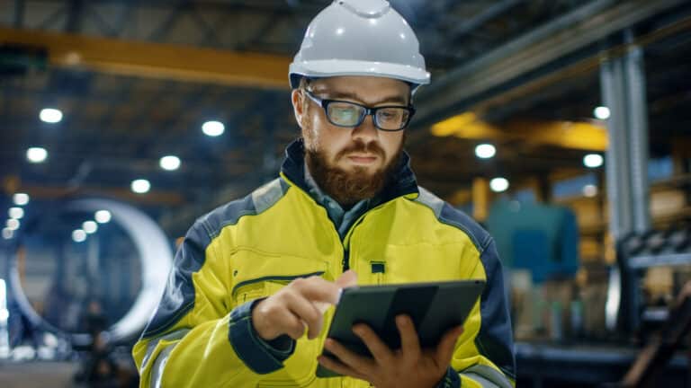 En person der arbejder i et industrielt miljø, fabrik eller produktionsanlæg. Han bruger en tablet til at registrere sit vedligehold data